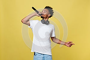 Young handsome African American Male Singer Performing with Microphone. Isolated over yellow gold background.