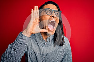 Young handsome african american man with dreadlocks wearing casual shirt and glasses shouting and screaming loud to side with hand