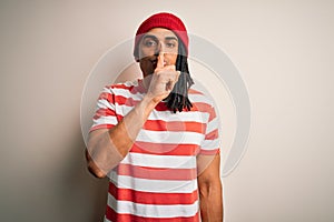 Young handsome african american man with dreadlocks wearing striped t-shirt and wool hat asking to be quiet with finger on lips