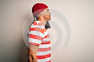 Young handsome african american man with dreadlocks wearing striped t-shirt and wool hat looking to side, relax profile pose with