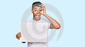 Young handsome african american man holding blank empty banner smiling happy doing ok sign with hand on eye looking through