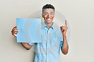 Young handsome african american man holding blue blank empty banner smiling with an idea or question pointing finger with happy