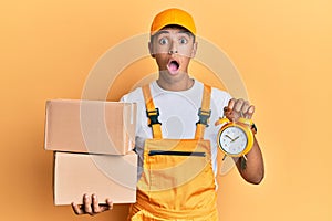Young handsome african american man holding delivery box and alarm clock for express service afraid and shocked with surprise and