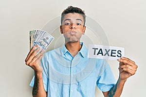 Young handsome african american man holding dollars and taxes paper puffing cheeks with funny face