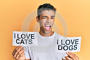 Young handsome african american man holding paper with i love cats and i love dogs phrase winking looking at the camera with sexy