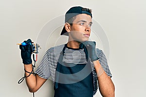 Young handsome african american man tattoo artist wearing professional uniform and gloves holding tattooer machine with hand on