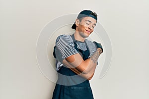 Young handsome african american man tattoo artist wearing professional uniform and gloves hugging oneself happy and positive,