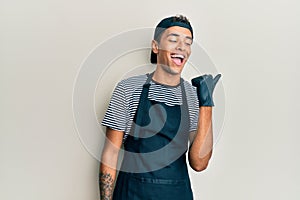 Young handsome african american man tattoo artist wearing professional uniform and gloves pointing thumb up to the side smiling