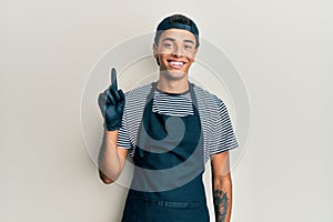 Young handsome african american man tattoo artist wearing professional uniform and gloves smiling with an idea or question