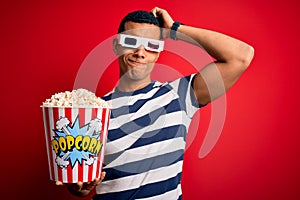 Young handsome african american man watching movie using 3d glasses eating popcorns confuse and wondering about question