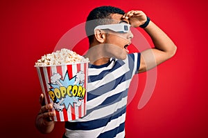Young handsome african american man watching movie using 3d glasses eating popcorns very happy and smiling looking far away with
