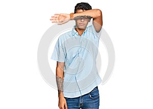 Young handsome african american man wearing casual clothes covering eyes with arm, looking serious and sad