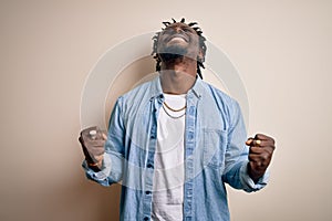 Young handsome african american man wearing casual denim shirt over white background very happy and excited doing winner gesture