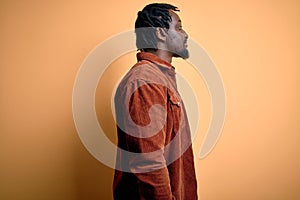 Young handsome african american man wearing casual jacket standing over yellow background looking to side, relax profile pose with