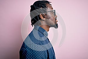 Young handsome african american man wearing casual shirt and glasses over pink background looking to side, relax profile pose with