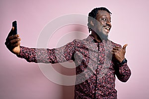 Young handsome african american man wearing casual shirt standing making selfie by camera pointing and showing with thumb up to