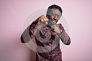 Young handsome african american man wearing casual shirt standing over pink background Punching fist to fight, aggressive and