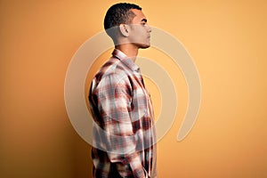 Young handsome african american man wearing casual shirt standing over yellow background looking to side, relax profile pose with