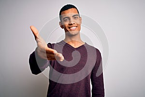 Young handsome african american man wearing casual sweater over white background smiling friendly offering handshake as greeting