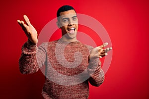 Young handsome african american man wearing casual sweater standing over red background looking at the camera smiling with open