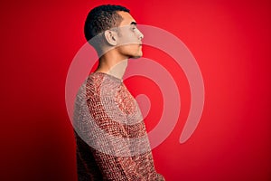 Young handsome african american man wearing casual sweater standing over red background looking to side, relax profile pose with