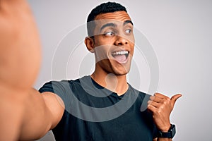 Young handsome african american man wearing casual t-shirt making selfie by camera pointing and showing with thumb up to the side