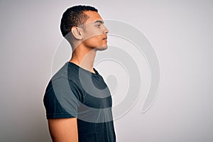 Young handsome african american man wearing casual t-shirt standing over white background looking to side, relax profile pose with