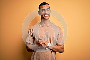 Young handsome african american man wearing casual t-shirt standing over yellow background with hands together and crossed fingers