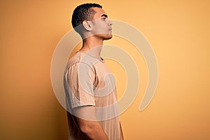 Young handsome african american man wearing casual t-shirt standing over yellow background looking to side, relax profile pose