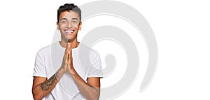 Young handsome african american man wearing casual white tshirt praying with hands together asking for forgiveness smiling