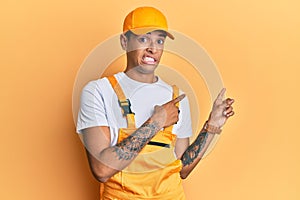 Young handsome african american man wearing handyman uniform over yellow background pointing aside worried and nervous with both