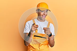 Young handsome african american man wearing handyman uniform over yellow background pointing fingers to camera with happy and