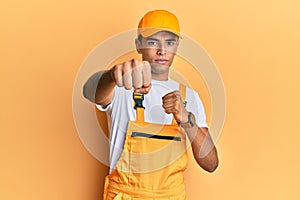 Young handsome african american man wearing handyman uniform over yellow background punching fist to fight, aggressive and angry