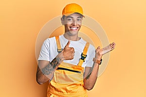 Young handsome african american man wearing handyman uniform over yellow background showing palm hand and doing ok gesture with