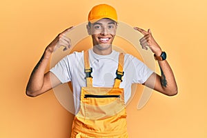 Young handsome african american man wearing handyman uniform over yellow background smiling pointing to head with both hands