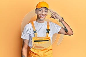 Young handsome african american man wearing handyman uniform over yellow background smiling pointing to head with one finger,