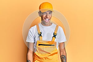 Young handsome african american man wearing handyman uniform over yellow background winking looking at the camera with sexy