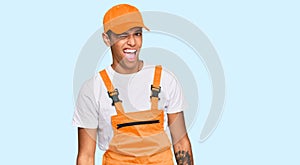 Young handsome african american man wearing handyman uniform winking looking at the camera with sexy expression, cheerful and