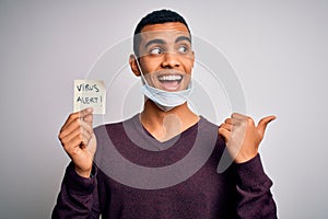 Young handsome african american man wearing medical mask holding virus alert reminder pointing and showing with thumb up to the