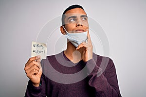 Young handsome african american man wearing medical mask holding virus alert reminder serious face thinking about question, very