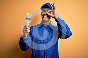 Young handsome african american painter man wearing uniform using painting brush with happy face smiling doing ok sign with hand