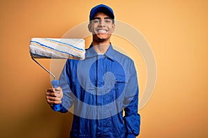 Young handsome african american painter man wearing uniform using painting roller with a happy face standing and smiling with a