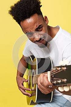 Young handsome African American retro styled guitarist playing acoustic guitar on yellow gold background.