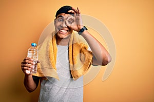 Young handsome african american sportsman wearing towel drinking bottle of water with happy face smiling doing ok sign with hand