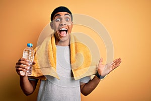 Young handsome african american sportsman wearing towel drinking bottle of water very happy and excited, winner expression