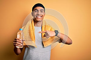 Young handsome african american sportsman wearing towel drinking bottle of water very happy pointing with hand and finger