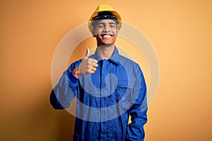Young handsome african american worker man wearing blue uniform and security helmet doing happy thumbs up gesture with hand