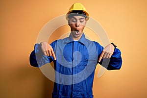 Young handsome african american worker man wearing blue uniform and security helmet Pointing down with fingers showing