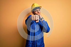 Young handsome african american worker man wearing blue uniform and security helmet Punching fist to fight, aggressive and angry