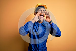 Young handsome african american worker man wearing blue uniform and security helmet Shouting angry out loud with hands over mouth